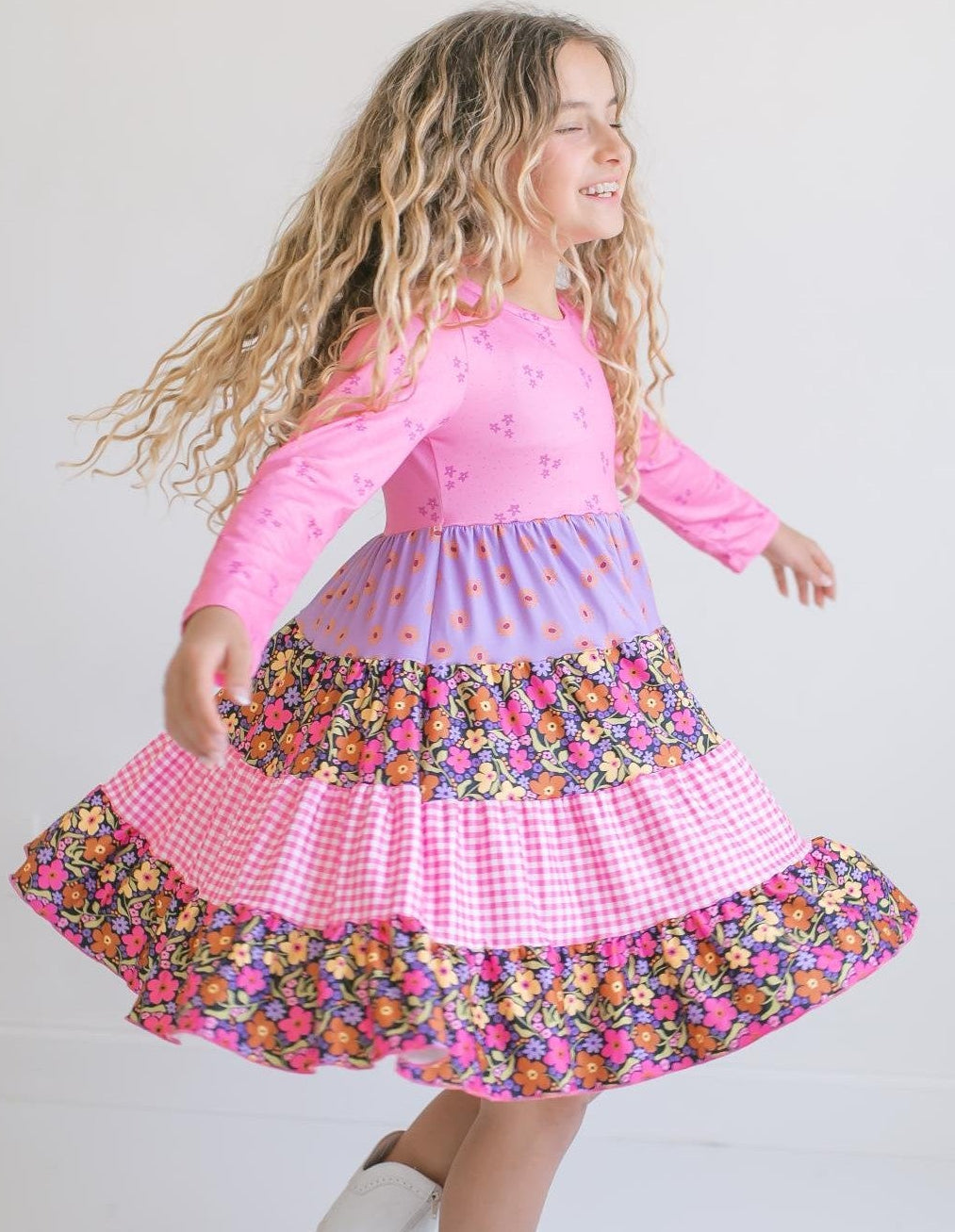 Girl wearing a bright pink floral long sleeve twirl dress with colorful tiered skirt.
