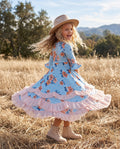Girl wearing a pastel blue and pink floral ruffle dress while twirling outdoors.