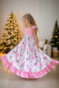 Girl wearing a pink deer Christmas nightgown with ruffle trim beside a decorated Christmas tree.